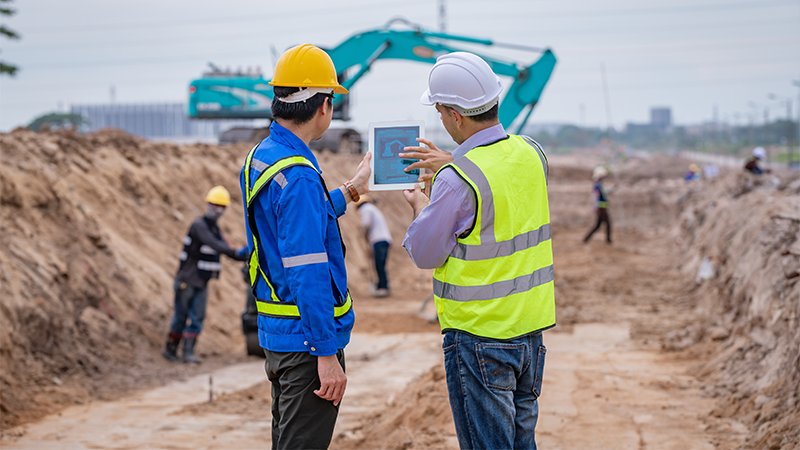 Et byggeområde hvor noen jobber med maskiner og noen sjekker en laptop
