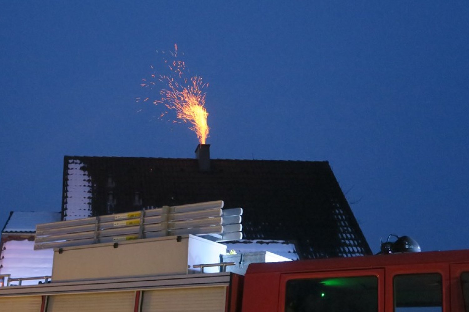 Gnister fyker ut av en skorstein på et hustak, med en brannbil i forgrunnen.
