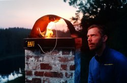 Grunnlegger av Safi Brannsikring, Ingolf Stokkeland, ser på et av produktene sine festet i toppen av en pipehatt, mens flammer kommer opp av pipa.