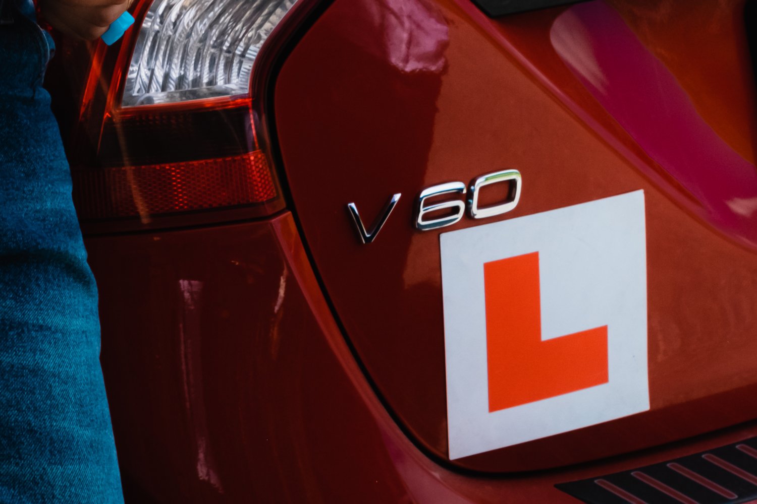 En jente står foran en rød bil med påmontert øvelseskjørings-L