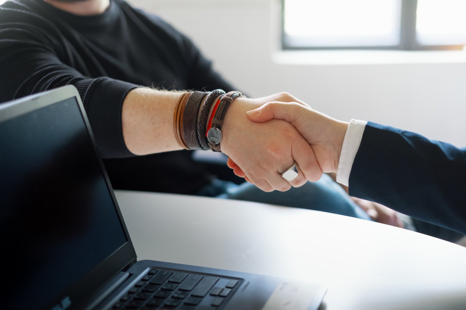 Håndtrykk mellom to personer, en ikledd dress, den andre svart genser.