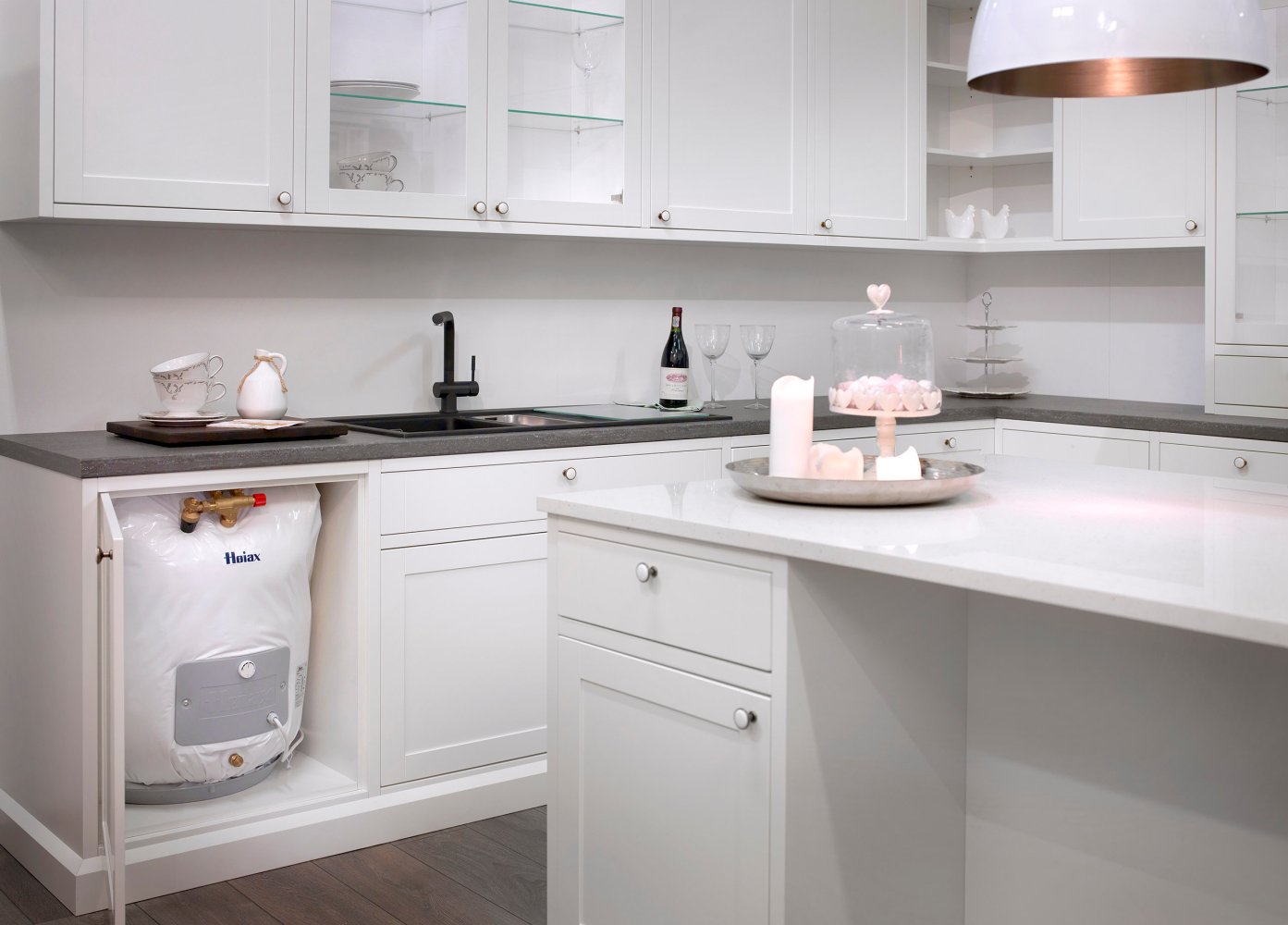 Kjøkken med åpent skap under vasken, hvor man ser en benkebereder installert.