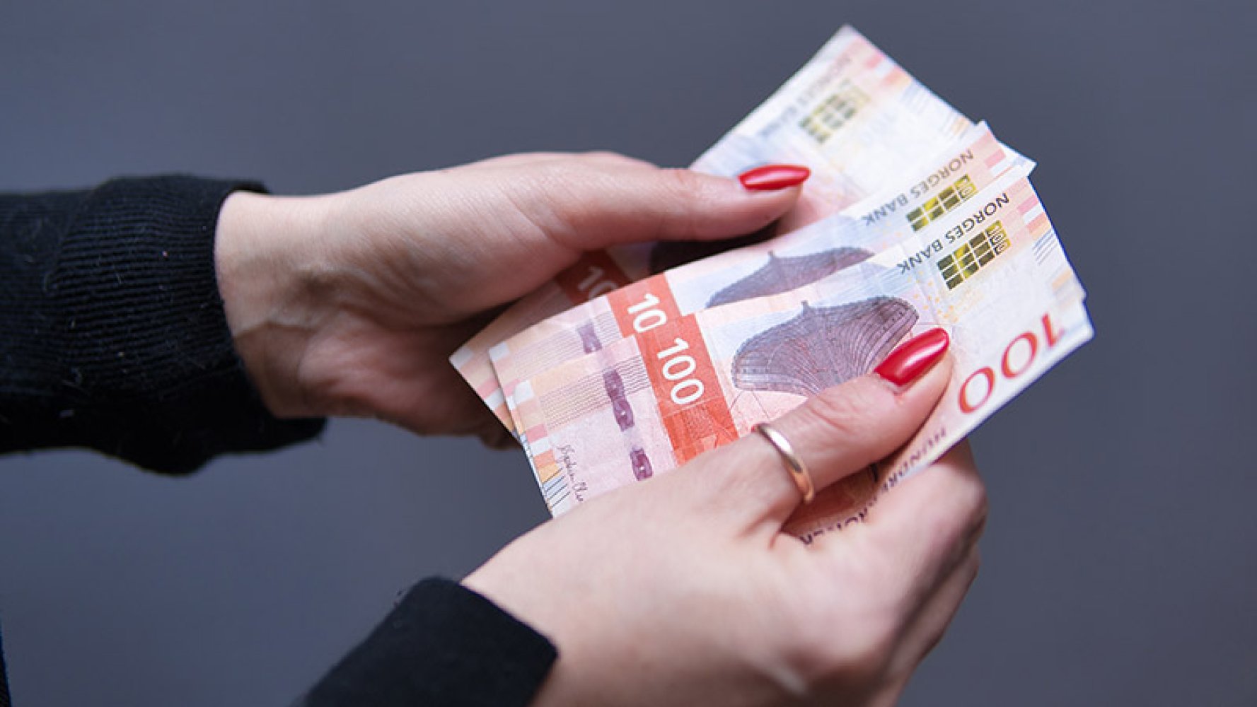 Dame som holder 100 kroner sedler i hånden.