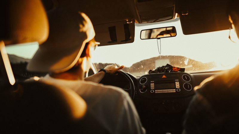 Ung sjåfør i førersetet på bil. sett fra baksetet.