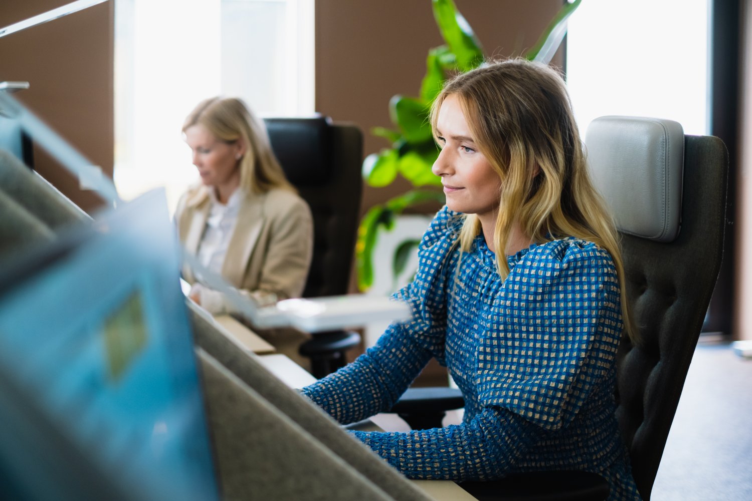 Dame sitter foran pc i åpent kontorlandskap.