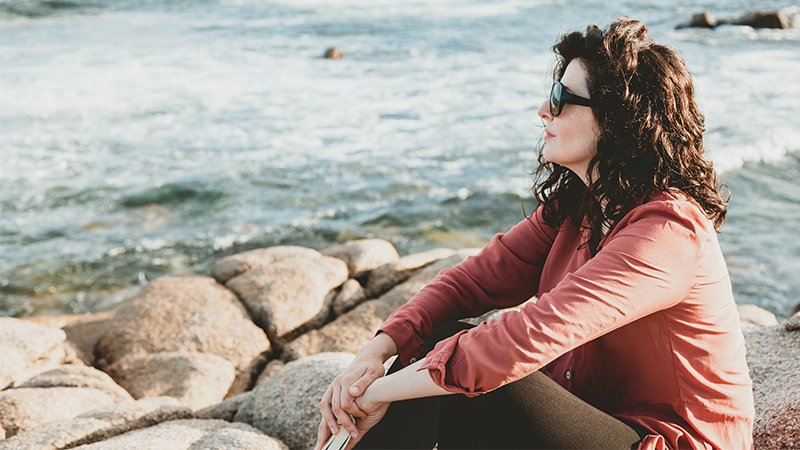 Dame på svaberg med bok og tankene.