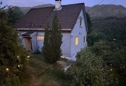 Blågrått hus med en skogskledd ås i bakgrunnen.