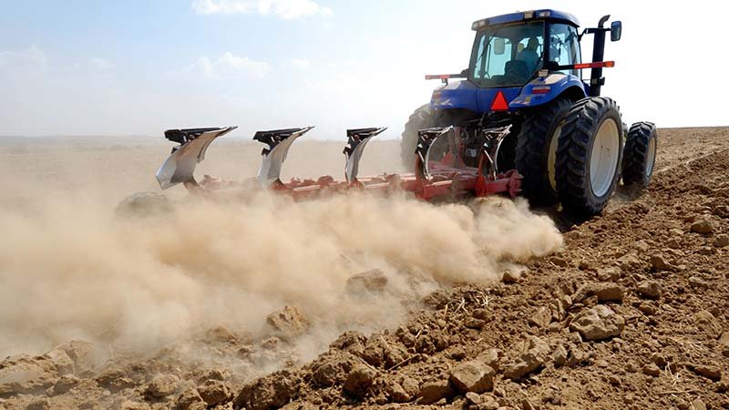 Traktor ploger på tørt jorde så støvet spruter