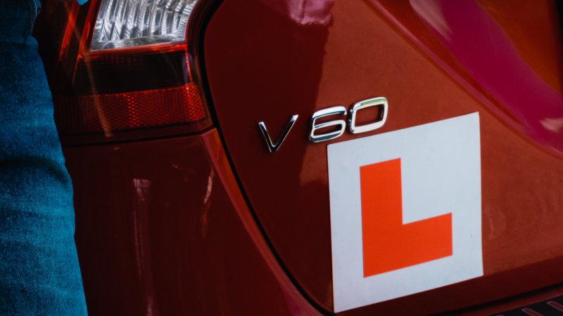 En jente står foran en rød bil med påmontert øvelseskjørings-L