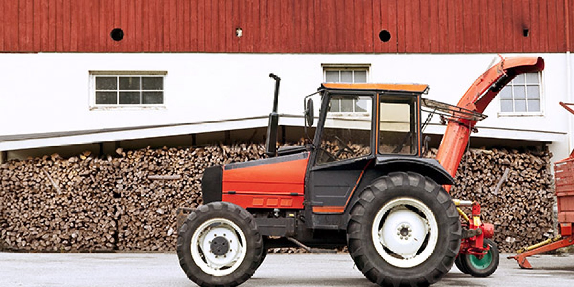 Rød traktor foran låve og vedstabel.