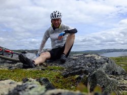 Rolf erik på sykkeltur. Sitter på stein. Utsikt over vann og natur