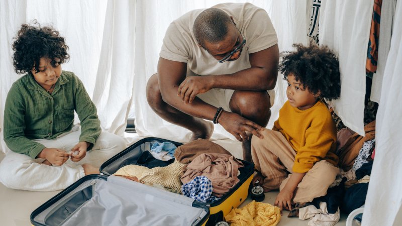 Far og to barn som pakker koffert.