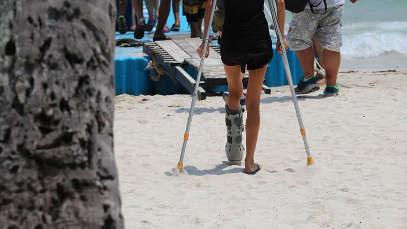 Dame på krykker på stranden.