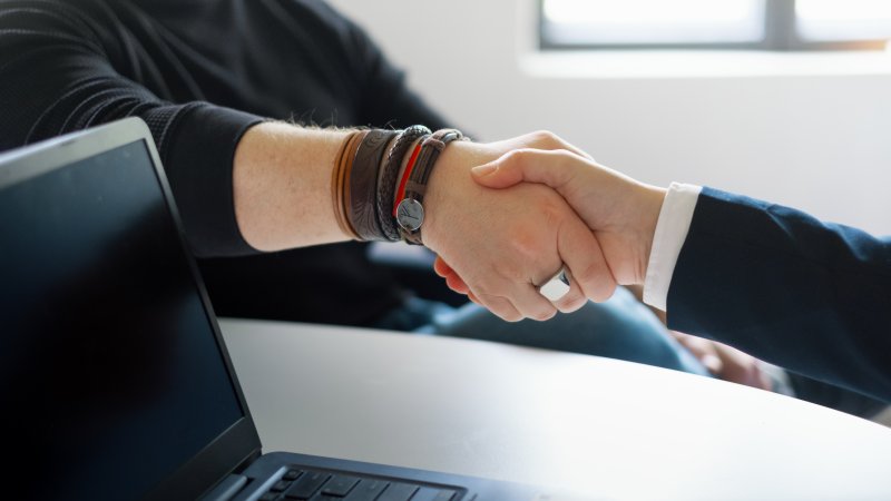 Håndtrykk mellom to personer, en ikledd dress, den andre svart genser.