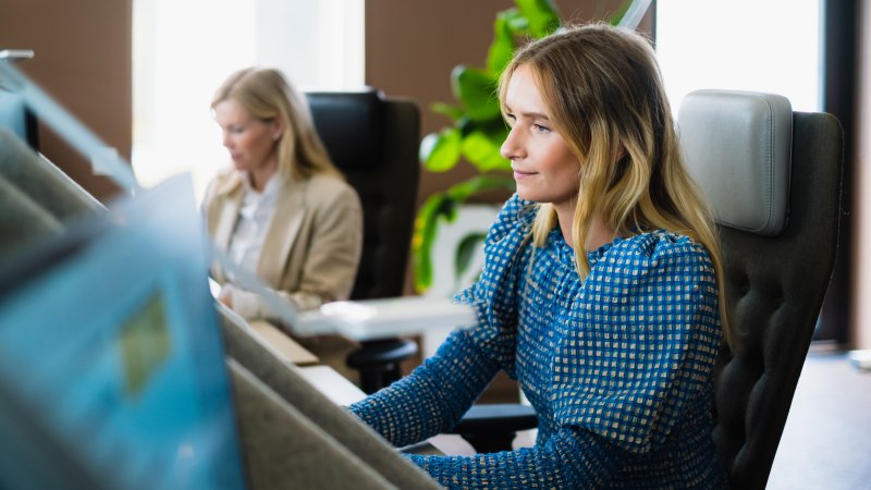 Dame sitter foran pc i åpent kontorlandskap.